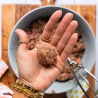A hand holding the scoop of meat mixture and rolling it into a perfect shape
