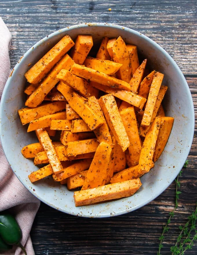Sweet potato fries in a large bowl tossed with olive oil and a seasoning blend before it goes into the air fryer.