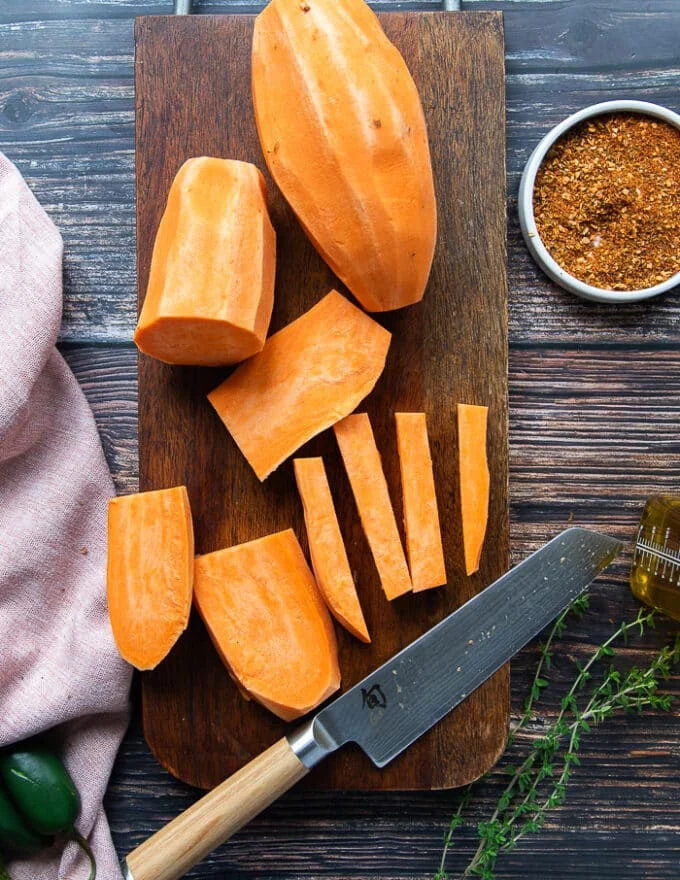 A hand cutting half an inch strips of the sweet potatoes to look like fries