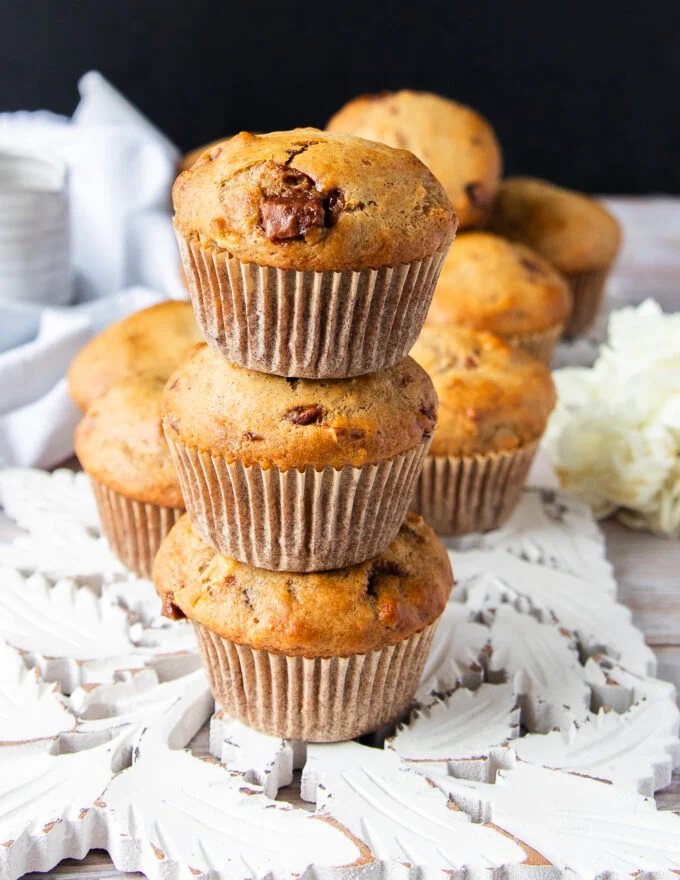 three banana bread muffins stacked up one over the other showing close up the golden tops with chocolate chunks studded and the fluffy tall bakery style muffins
