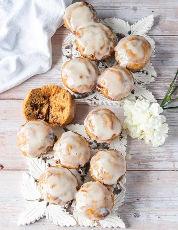 A full spread of cream cheese glazed moist banana bread muffins on a table with one of them cut in half showing the fluffy texture
