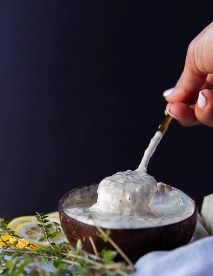 A hand holding a spoon in to the garlic parmesan sauce showing the creamy consistency of the sauce