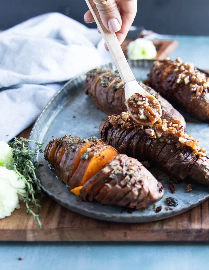 A spoon adding some extra cinnamon sugar pecan butter over the sweet flavored hasselback sweet potatoes