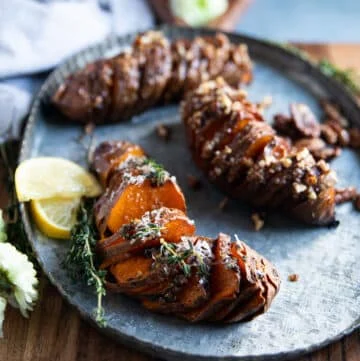 hassleback sweet potatoes on a serving platter showing the thin slices and the layers of herbs or pecans flavoring for a sweet and savory version