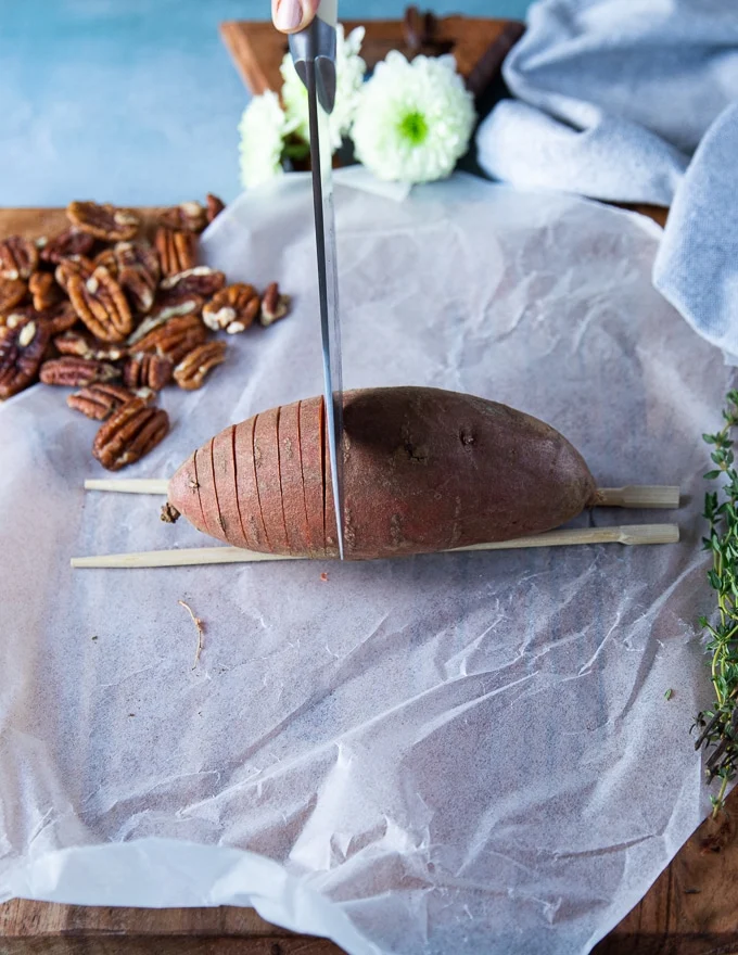 A sharp knife cutting through thin slices of the sweet potato