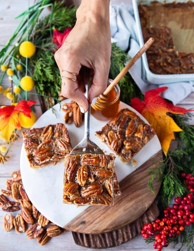 A hand holding a square spatula removing the first square from the pan of the pecan pie bars recipe