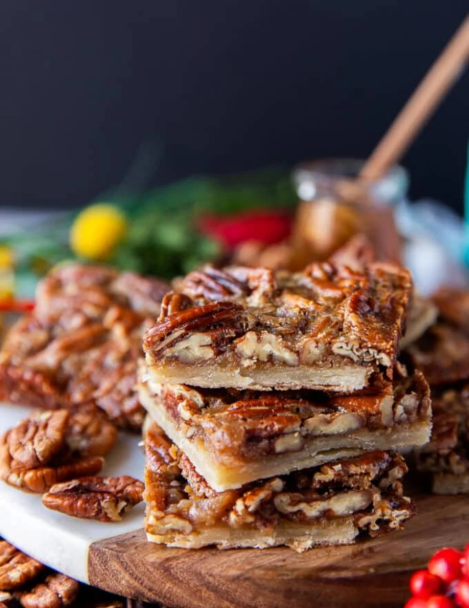 Stacked up pecan pie bars showing the close up texture and layers of crust, a thin caramel filling and lots of pecans