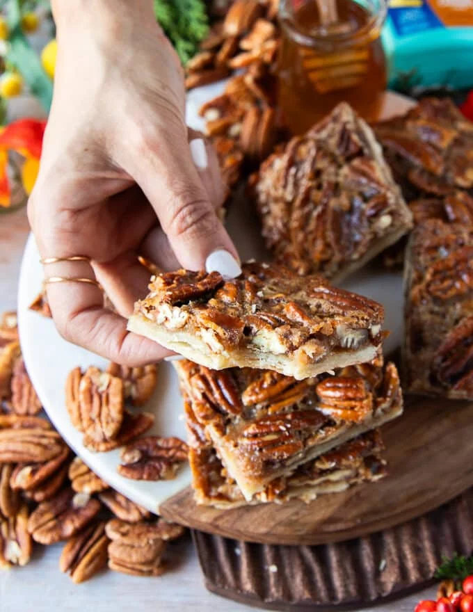 A hand holding a pecan pie bar square and taken a bite showing the close up texture of the bars