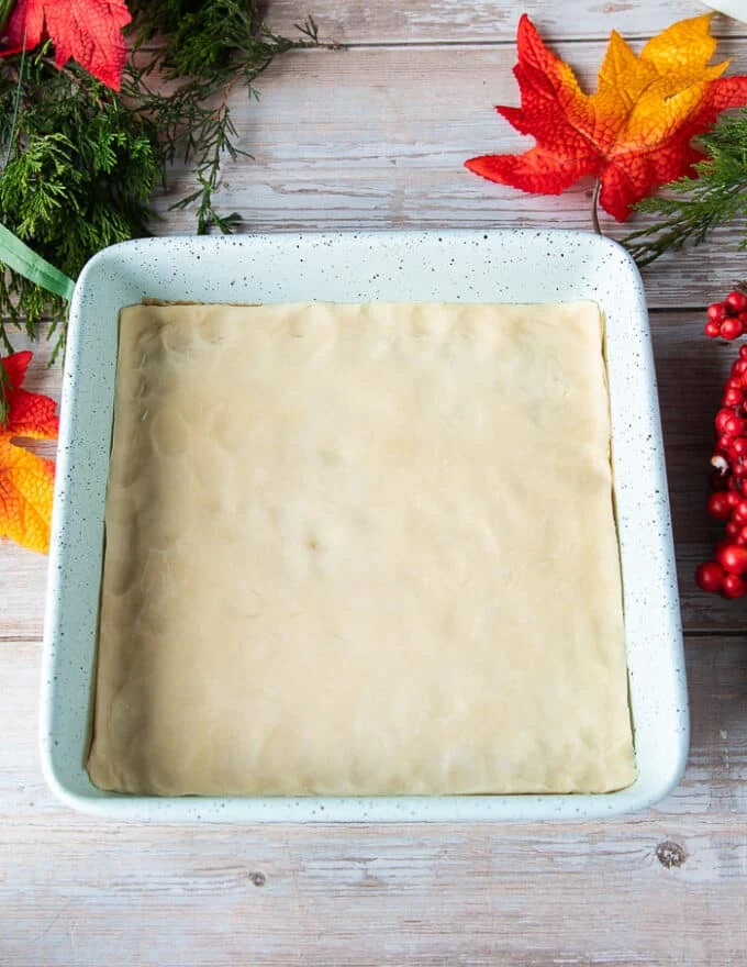The shortbread crust or pie dough fitted into a 9 inch square pan ready to bake before making the pecan pie bars filling