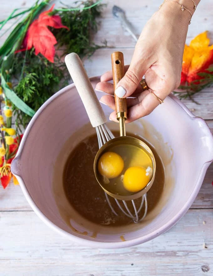A hand ready to pour the eggs one at a time into the warm caramel mixture while the other hand holding a whisk to whisk continuously