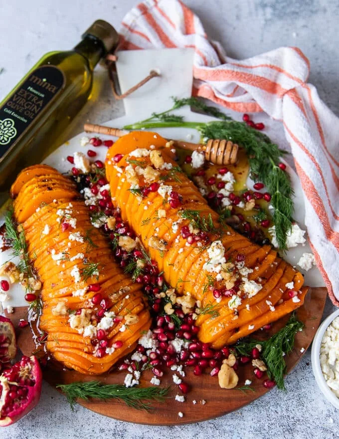 Two halves of roasted butternut squash sliced and topped with feta cheese, and walnuts