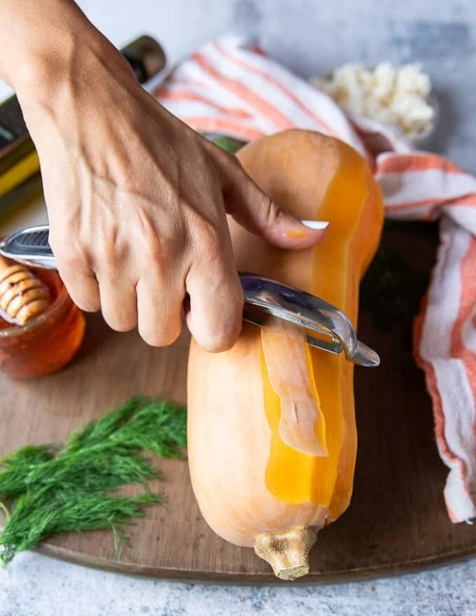 A hand peeling the butternut squash using the peeler