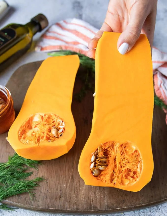 A hand holding a cut up half of butternut squash showing the seeds and texture of the veggie