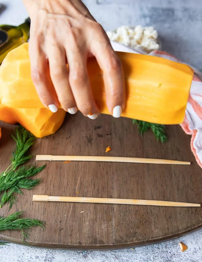 A hand showing how to cut the squash by placing one half on the wooden board
