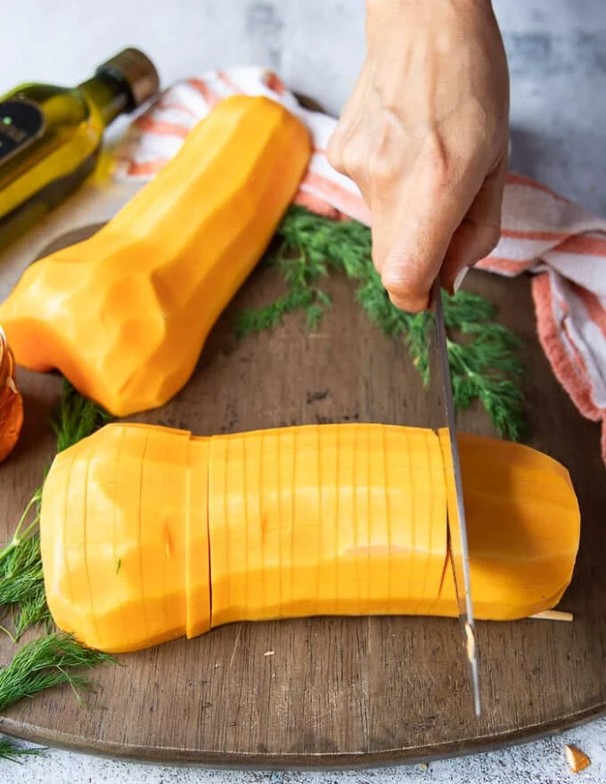 A knife thinly slicing the butternut squash