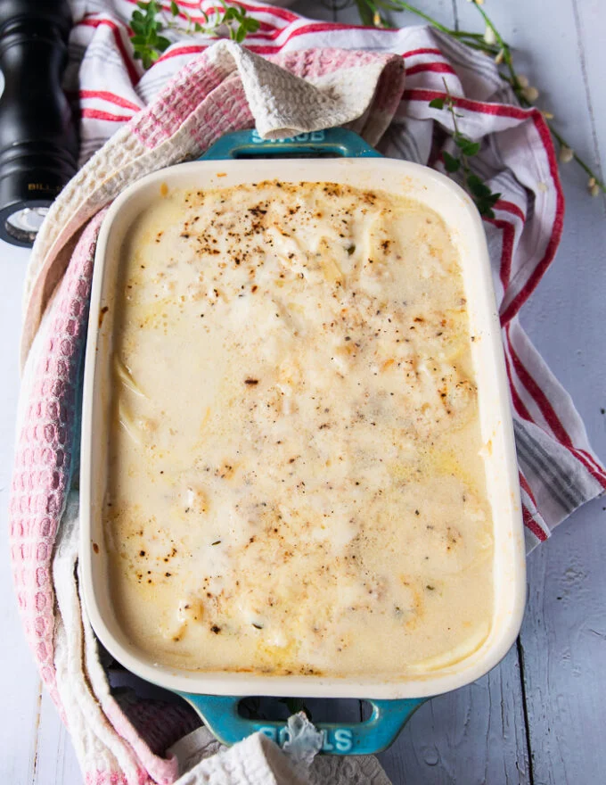 The scalloped potatoes uncovered halfway through baking showing how the potatoes have released some moisture into the sauce and the dish is retuned back to the oven