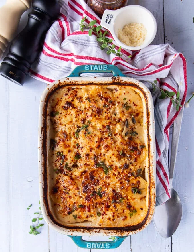 A final dish of scalloped potatoes on a white table with some salt and pepper extra on the side and a tea towel