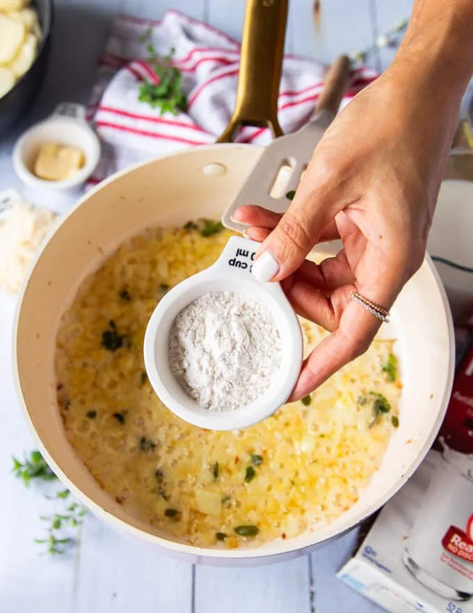 A hand holding the flour to be added to the sauce once the onions are ready