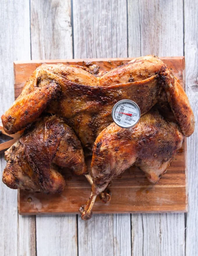 The spatchcock turkey removed to a cutting board and a meat thermometer inserted in the turkey.