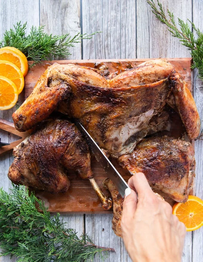 A hand holding a sharp knife and starting to carve the spatchcock turkey by beginning to cut the thighs