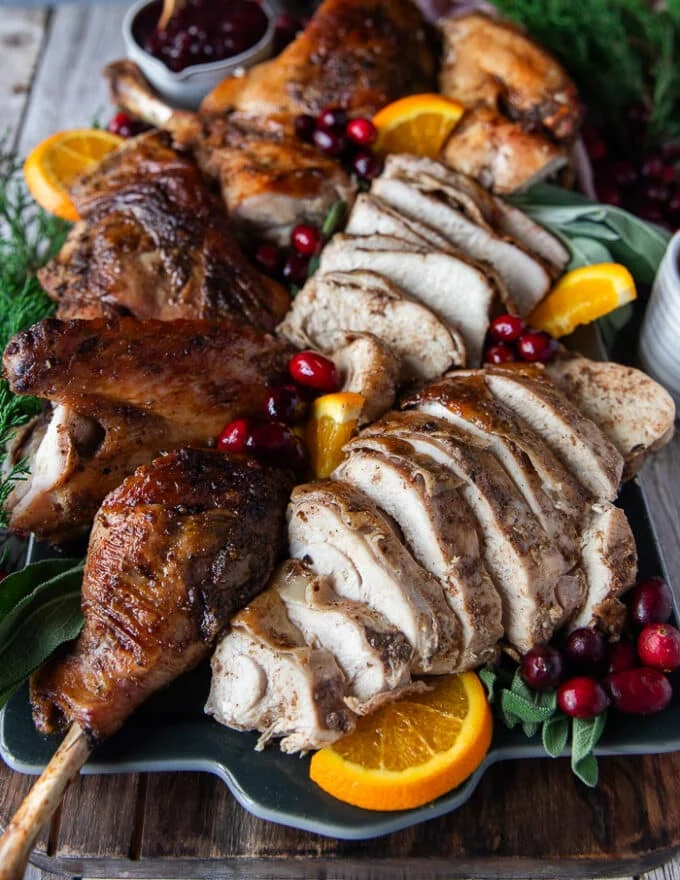 thinly sliced turkey breast arranged on a serving plater along with the other parts of the carved turkey
