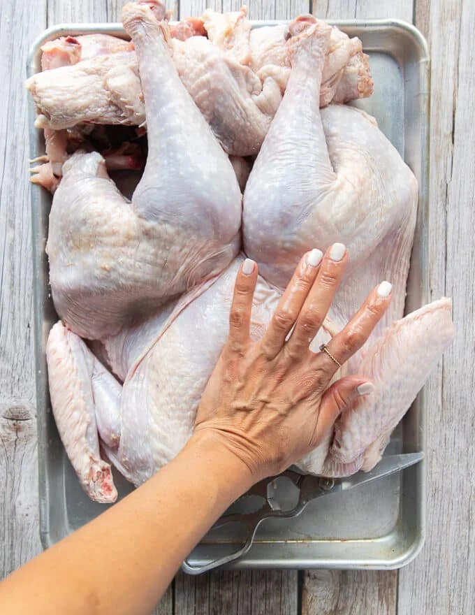 A hand pressing firmly on the breast bone of the turkey to crack it and flatten the turkey