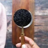 A hand holding a cup of wild black rice showing it and preparing it to cook