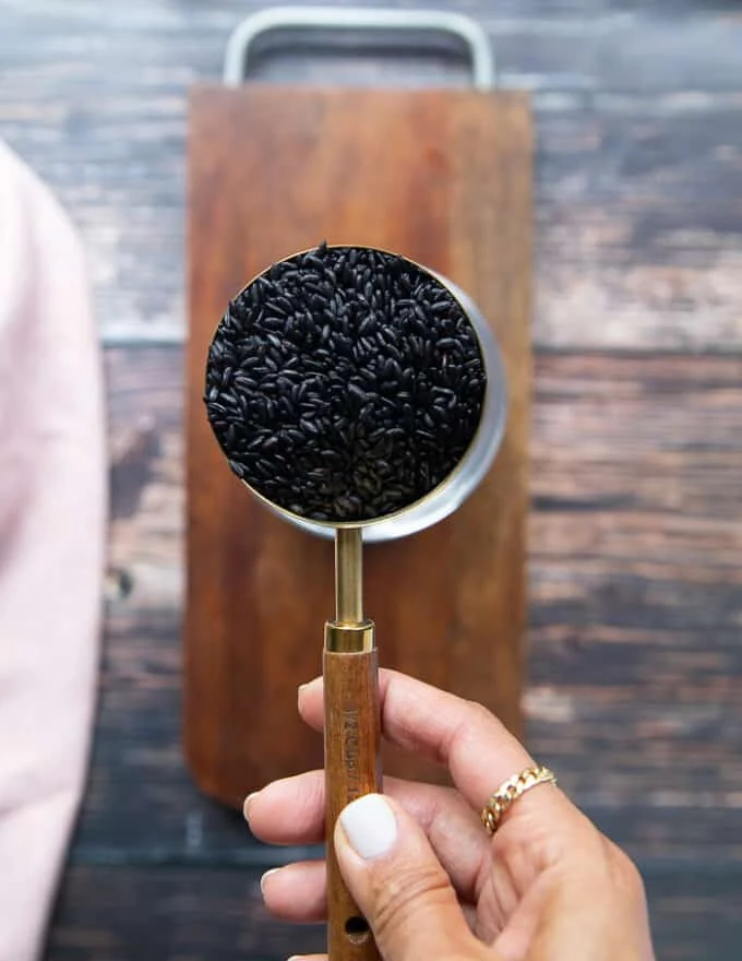 A hand holding a cup of wild black rice showing it and preparing it to cook
