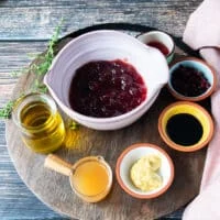 Ingredients for sweet potato salad dressing in a wooden board including a bowl of cranberry sauce, a bowl of mustard, some vinegar in a bowl, some balsamic vinegar in a bowl, some olive oil, and dried cranberries in a bowl