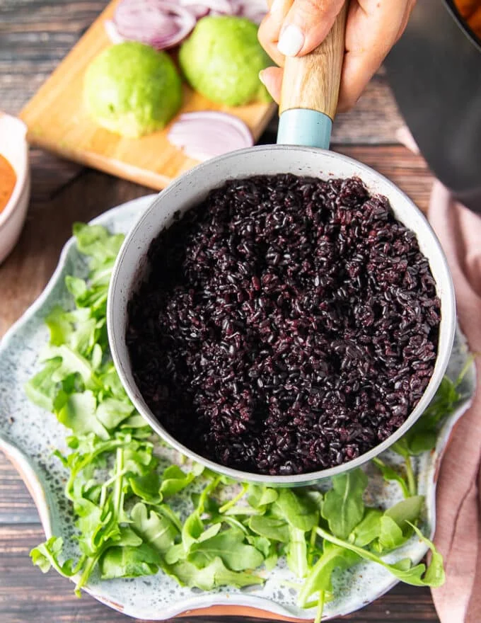 The cooked wild rice in a pan being added over the plate of arugula