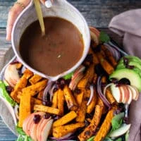 A hand drizzling the cranberry sauce over the sweet potato salad