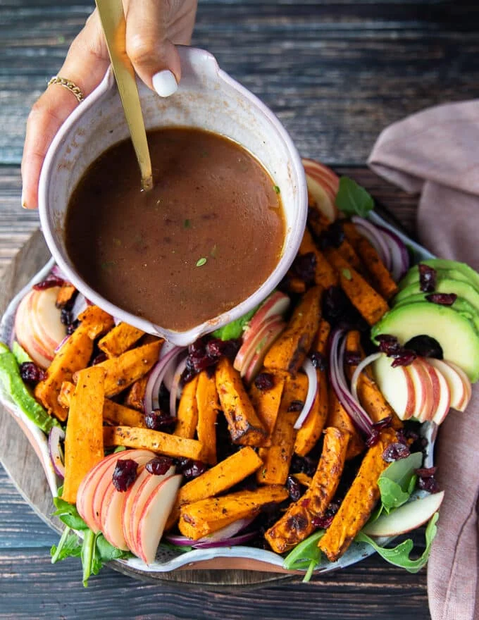 A hand drizzling the cranberry sauce over the sweet potato salad