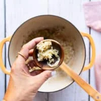 A hand holding the minced garlic in a bowl ready to add to the soup