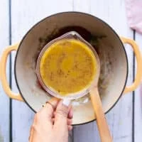 A hand holding the stock in a bowl ready to add to the soup