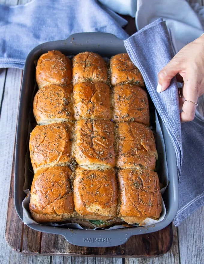 Turkey sliders out of the oven in the pan and a hand holding a kitchen towel to show them