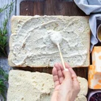 A hand spreading a generous amount of the garlic parmesan sauce at the bottom and top halves of the bread