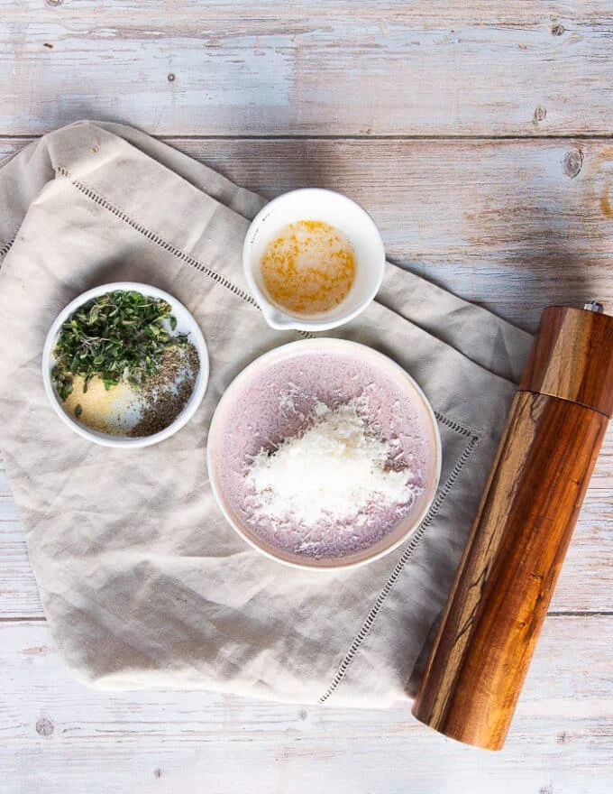 Ingredients for garlic parmesan butter to toss in the mushrooms including: a bowl of melted butter, a plate of grated parmesan cheese, a plate of fresh thyme/oregano, some salt and pepper and garlic powder