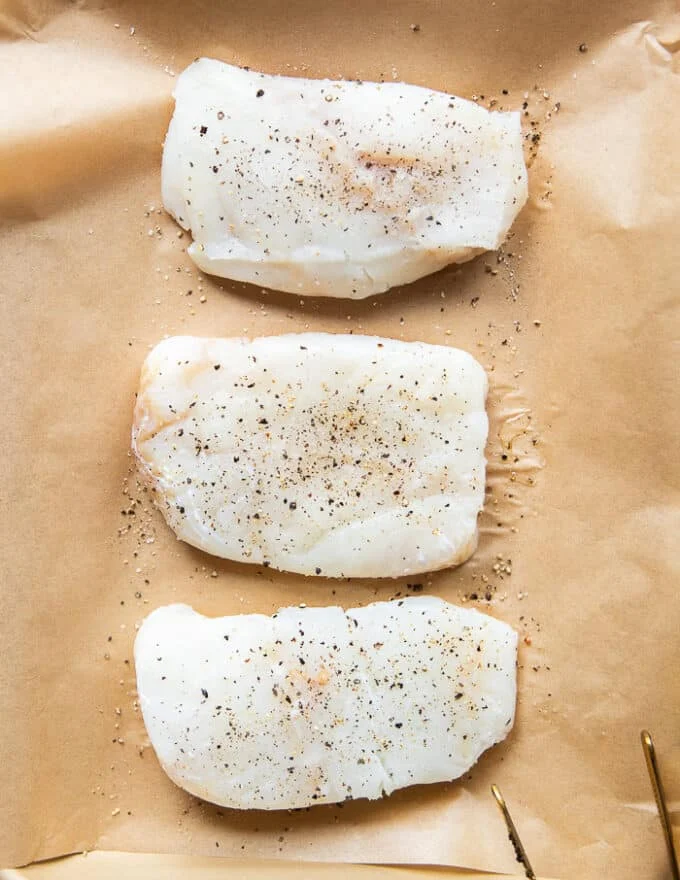 cod fillets on a baking sheet lined with parchment paper seasoned on both sides with salt and pepper