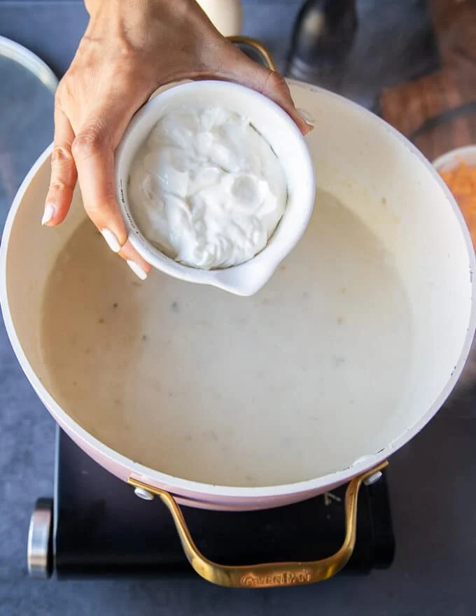 A hand adding in the sour cream into the baked potato soup