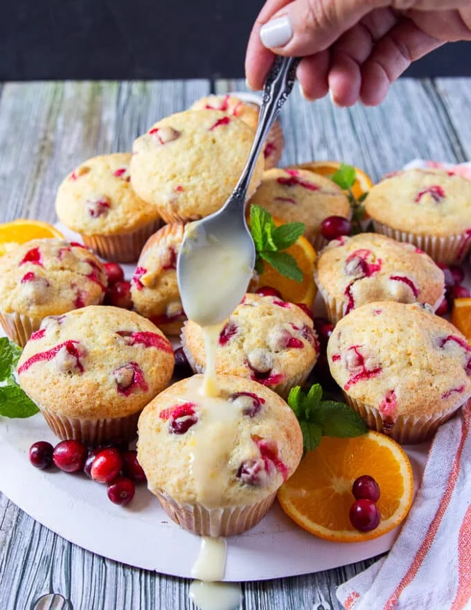 A hand holding a spoon and drizzling the glaze right over the muffins