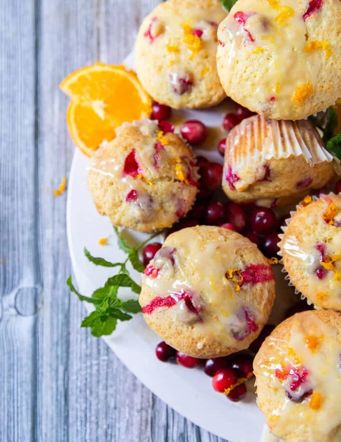 Close up top view of half the board of orange cranberry muffins focusing on one muffin very close showing the texture and glaze
