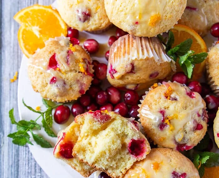 A board of cranberry orange muffins glazed and one of the muffins is cut into half to show closely the soft and fluffy texture of the muffins