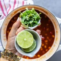 A hand holding a handful of cilantro and a lime cut in half ready to squeeze it in as the taco soup recipe is complete