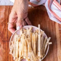 A hand holding a plate of tortillas cut into thin strips