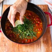 chicken tortilla soup is ready and a hand is squeezing lime over it in the pot and a added cilantro
