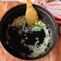 One large pot with onions and jalapeños sautéing and a wooden spoon mixing it in