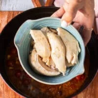 A hand holding in the cooked chicken and ready to add it into the soup