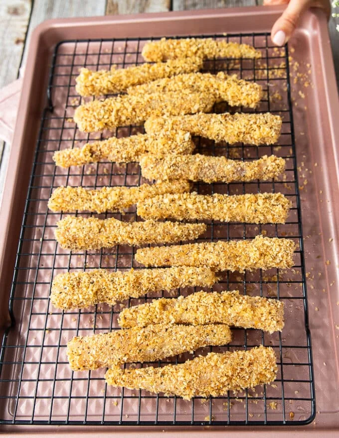 The coated fish fingers in breadcrumbs arranged on a cooling rack on the baking sheet ready to bake