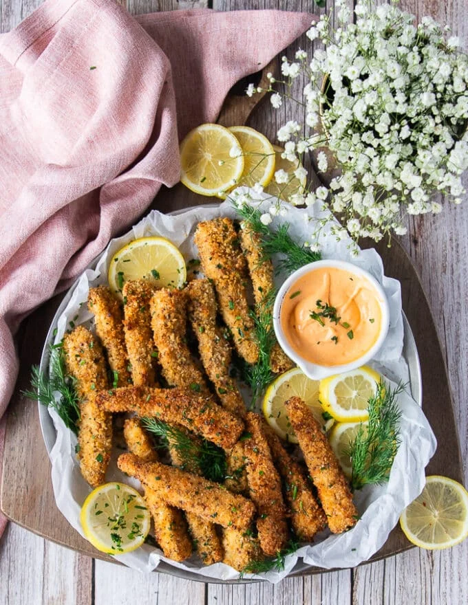 A large plate of fish fingers out of the air fryer or oven with a dip bowl