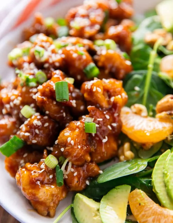close up of the orange chicken served sprinkled with some sesame seeds and green onions chopped